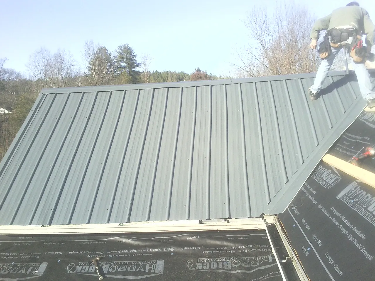 Crew installing dark green standing seam panels over synthetic underlayment in Oak Park