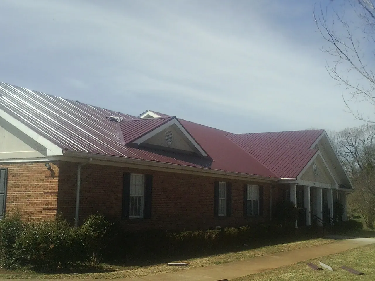 Red metal roof with gabled entries on a long brick building, from a Hail Damage Roof Repair job in Oak Park